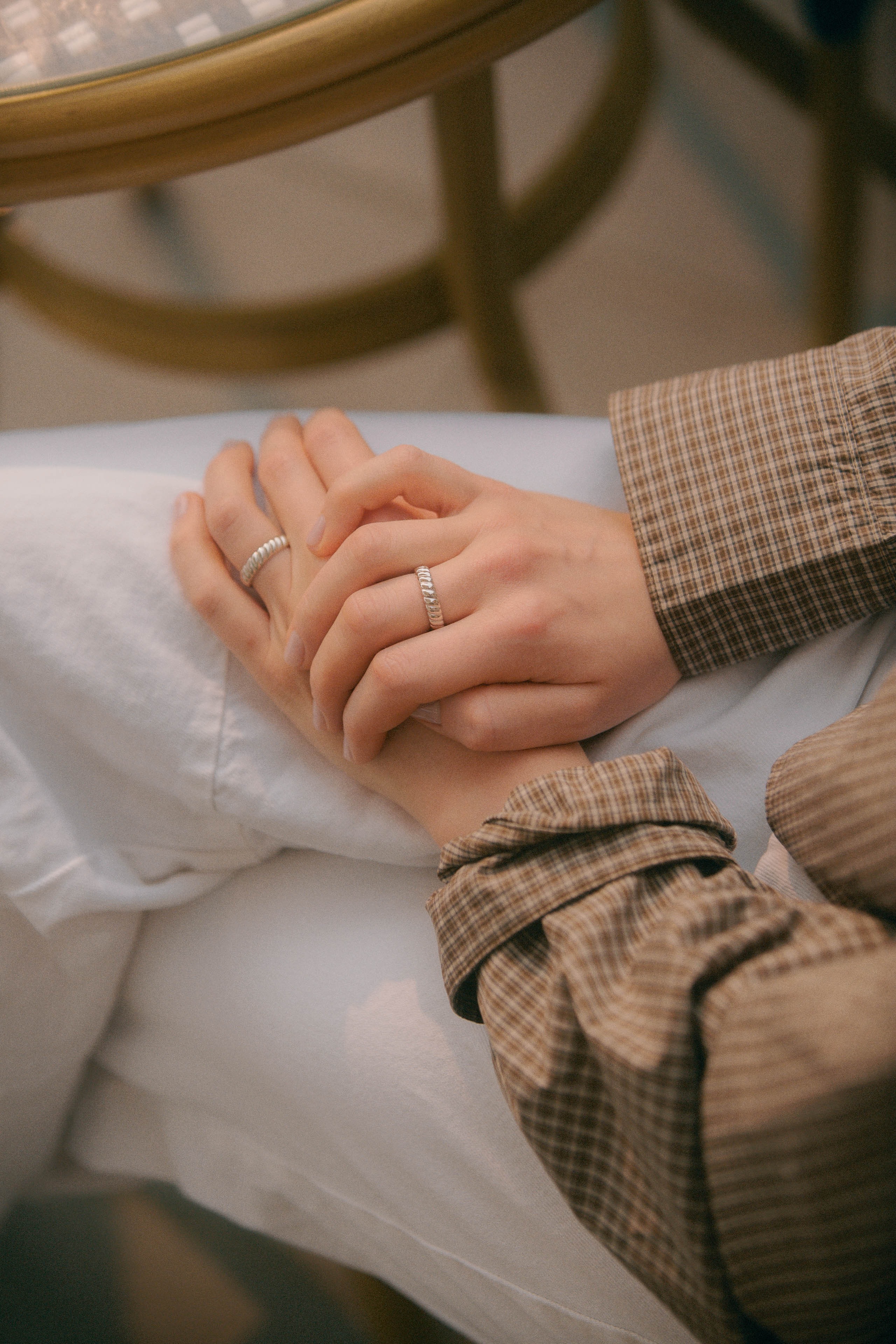 Close-up of two hands holding each other, wearing rings, with a blurred background.