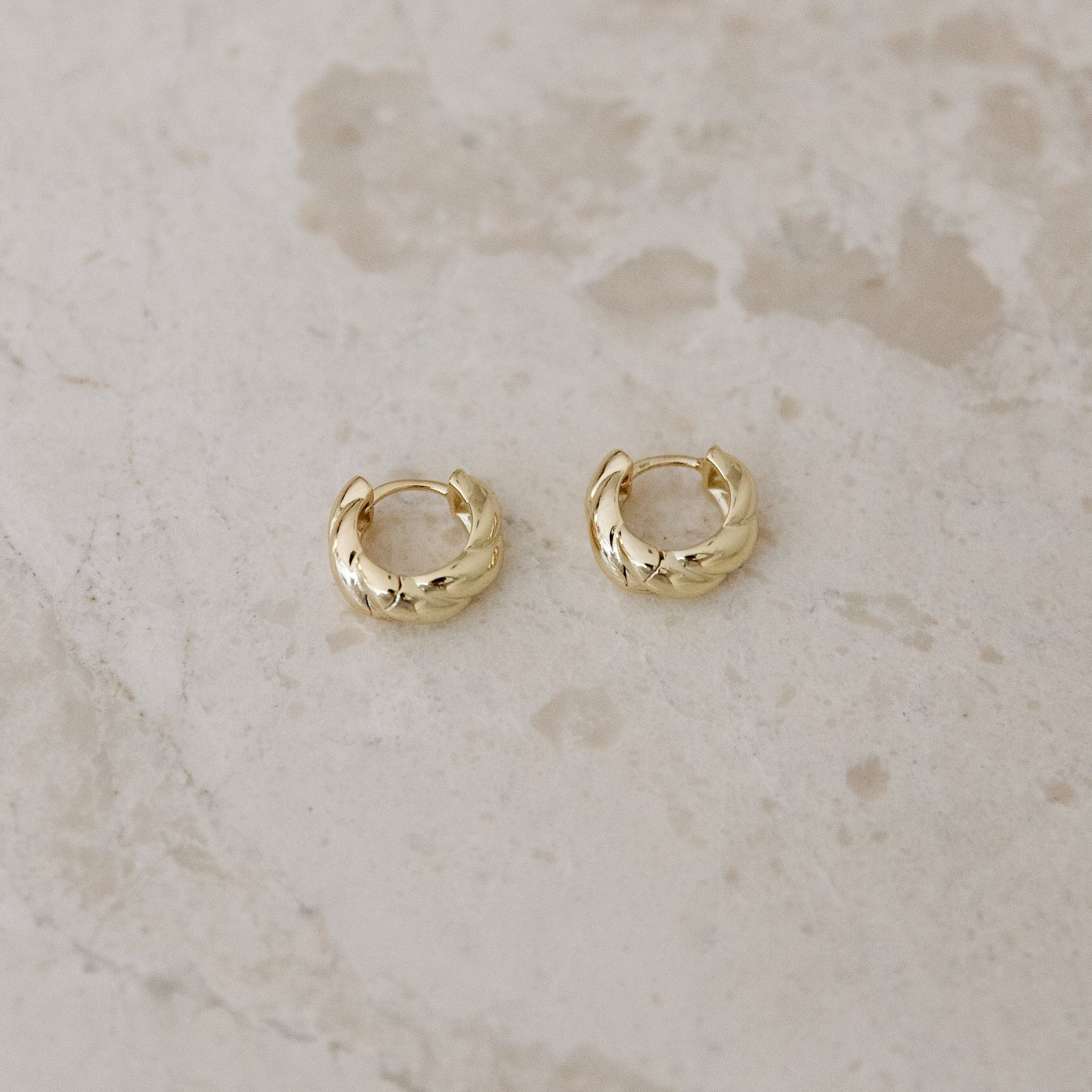 Gold hoop earrings on a light marble background