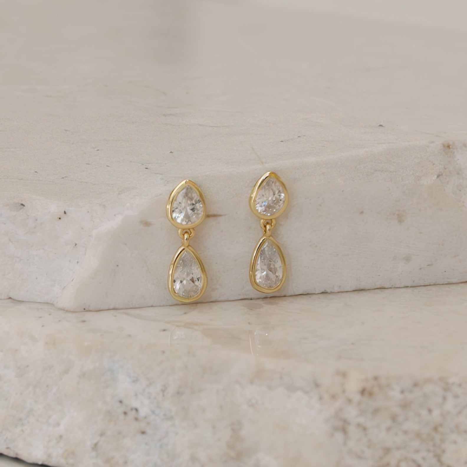 Gold earrings with clear stones on a stone surface