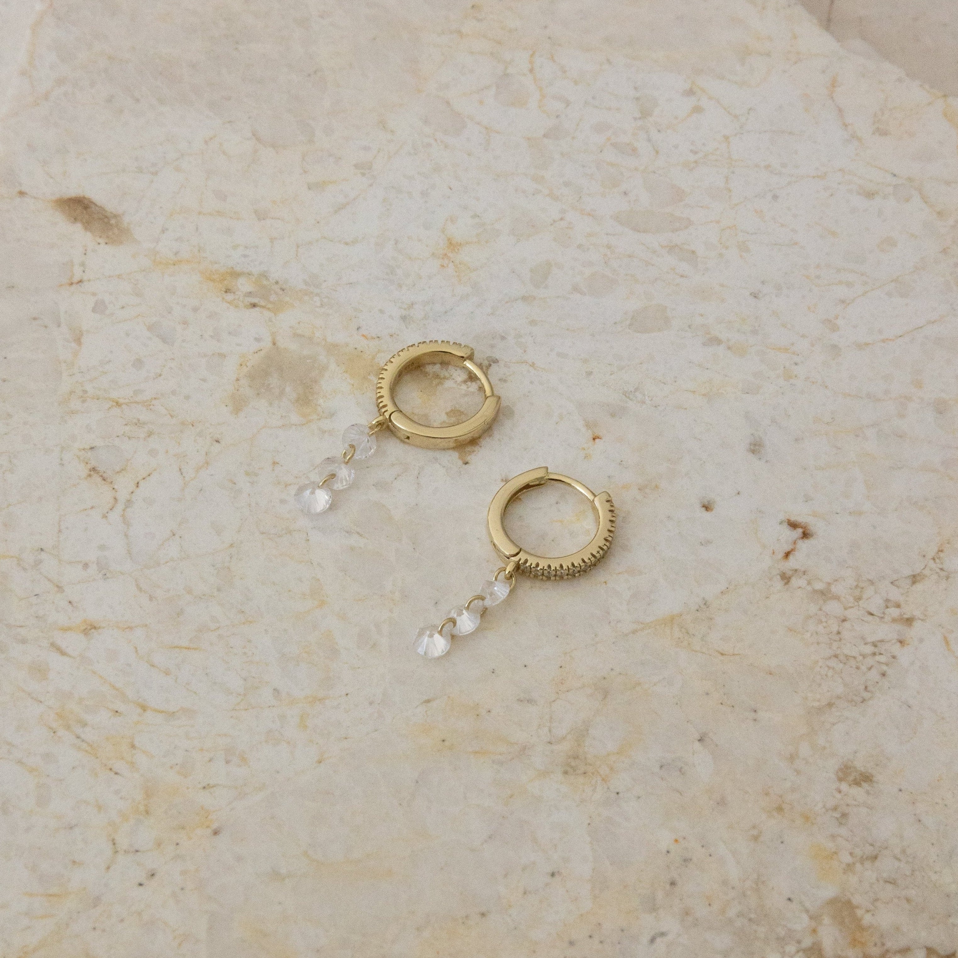 Gold hoop earrings with pearl-like beads on a beige marble surface