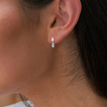 Close-up of an ear wearing a silver earring with a clear gemstone.