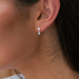 Close-up of an ear wearing a silver earring with a clear gemstone.