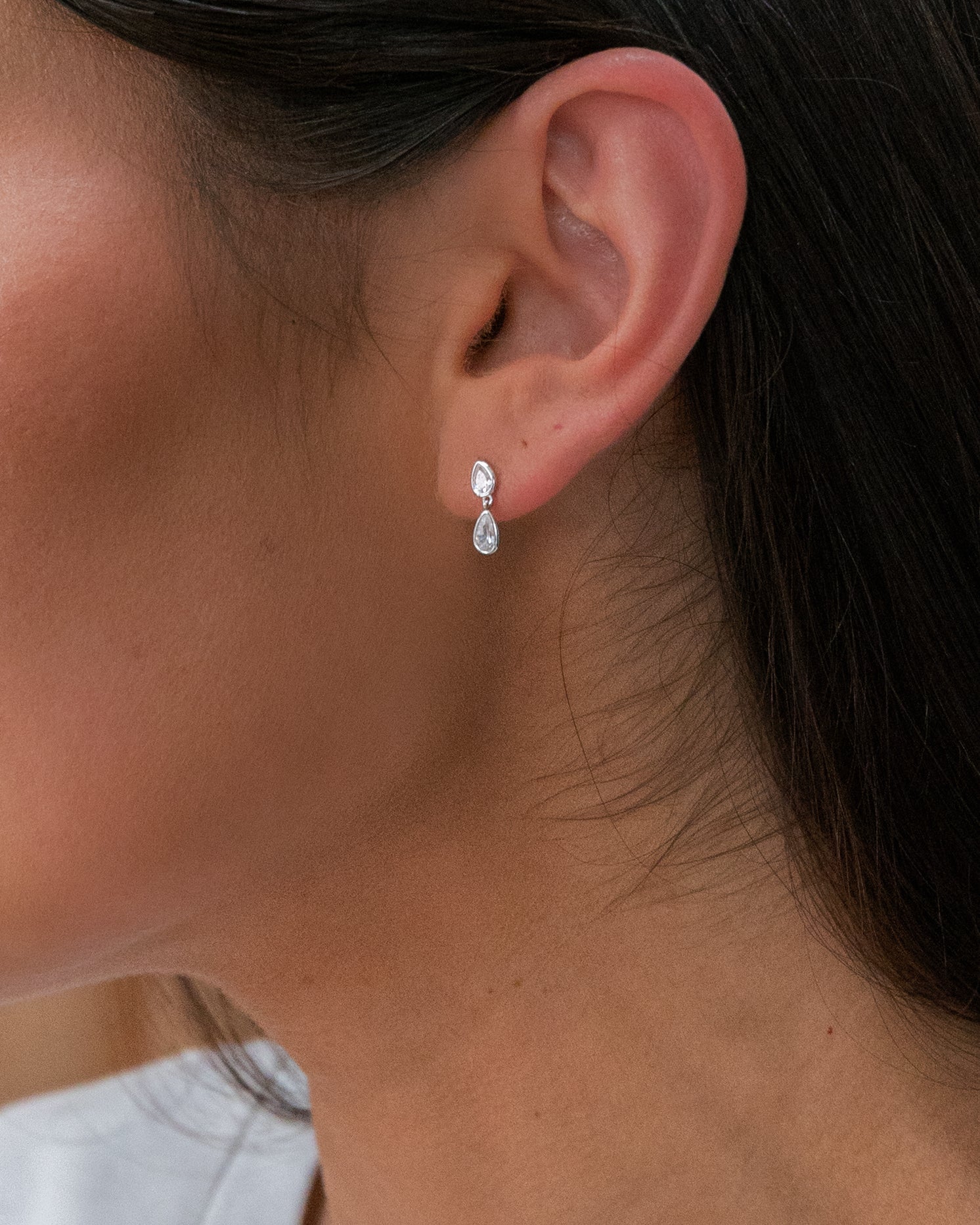 Close-up of an ear wearing a silver earring with a clear gemstone.
