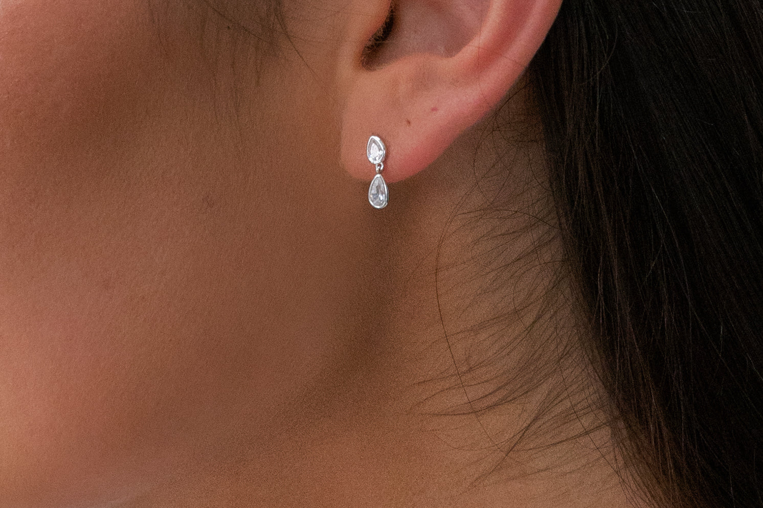 Close-up of an ear wearing a silver earring with a clear gemstone.