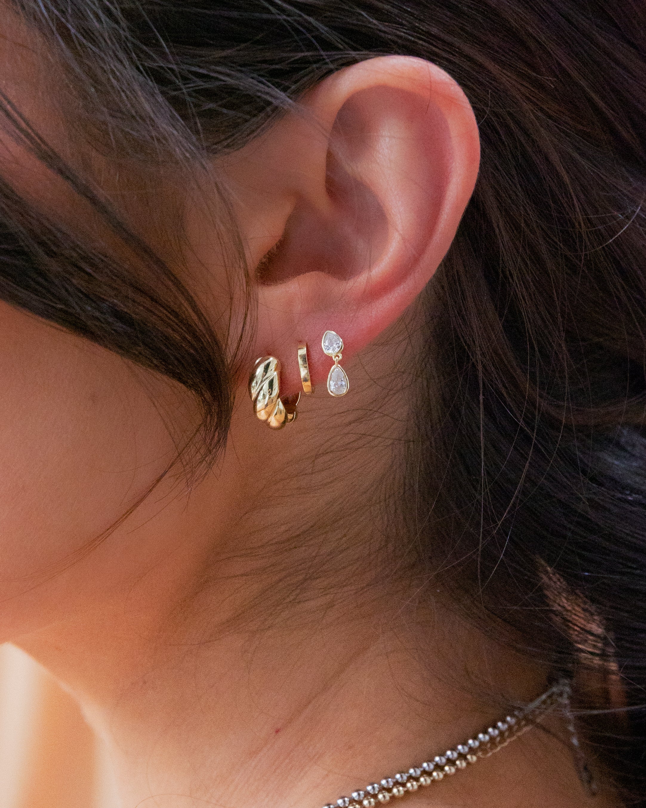Close-up of an ear wearing three earrings with a blurred background