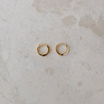 Gold hoop earrings on a textured beige surface