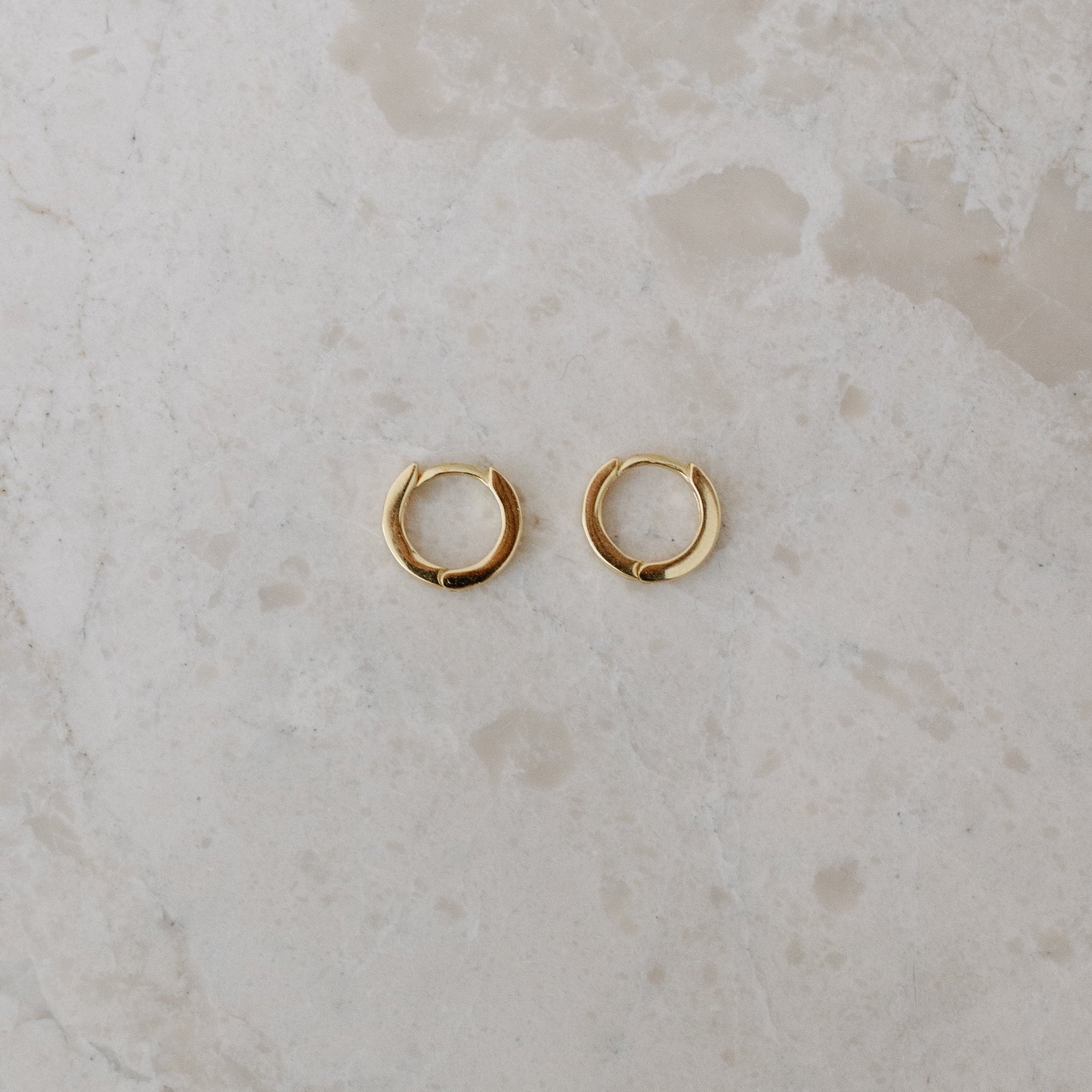 Gold hoop earrings on a textured beige surface