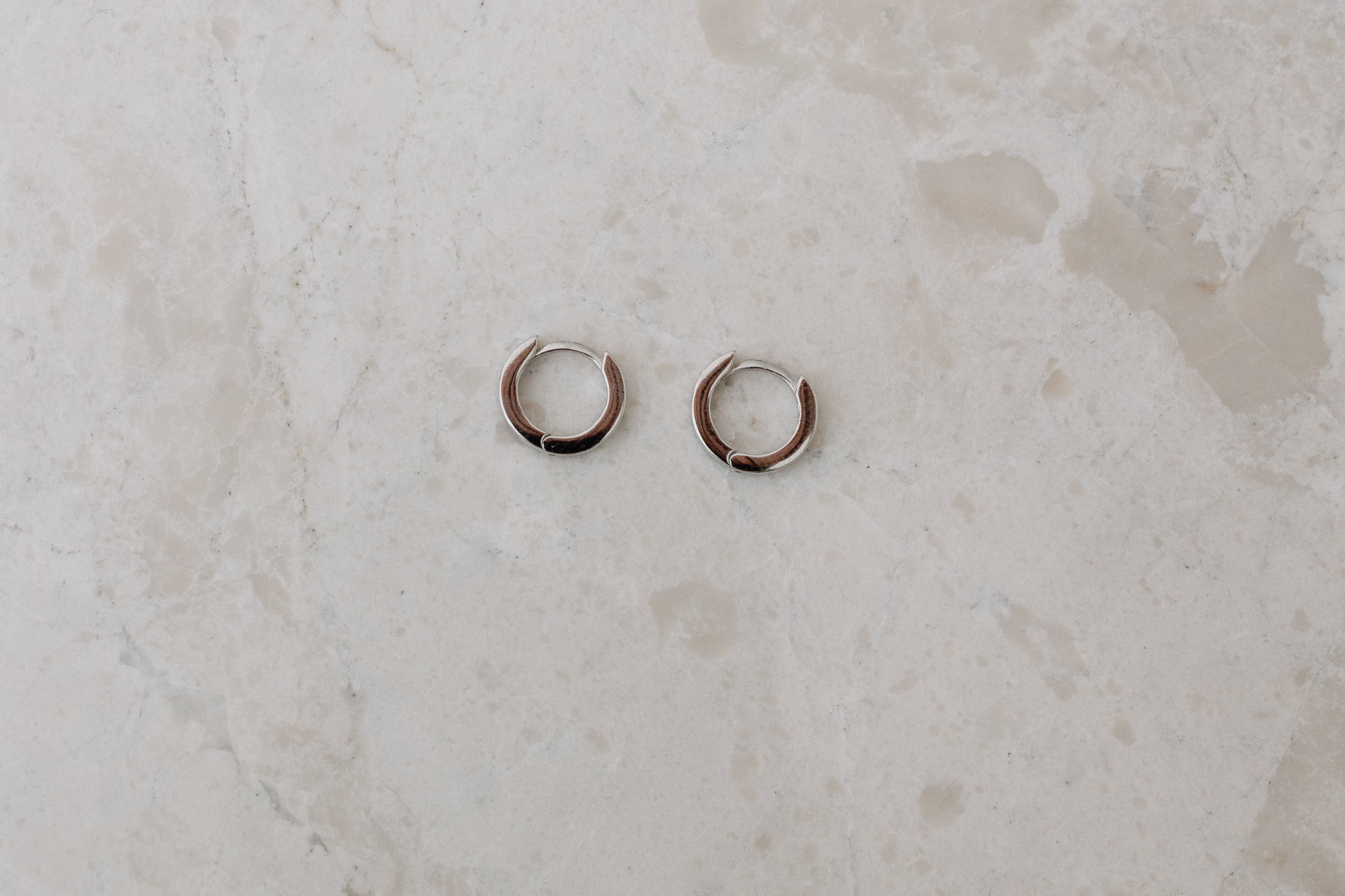 Two gold hoop earrings on a marble surface