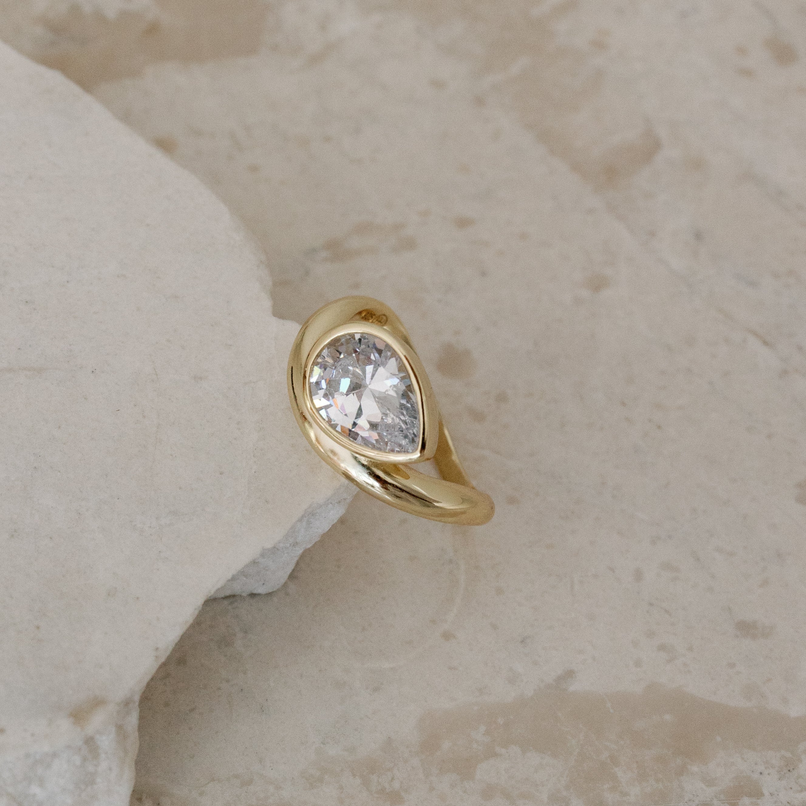 Gold ring with a diamond on a textured beige surface