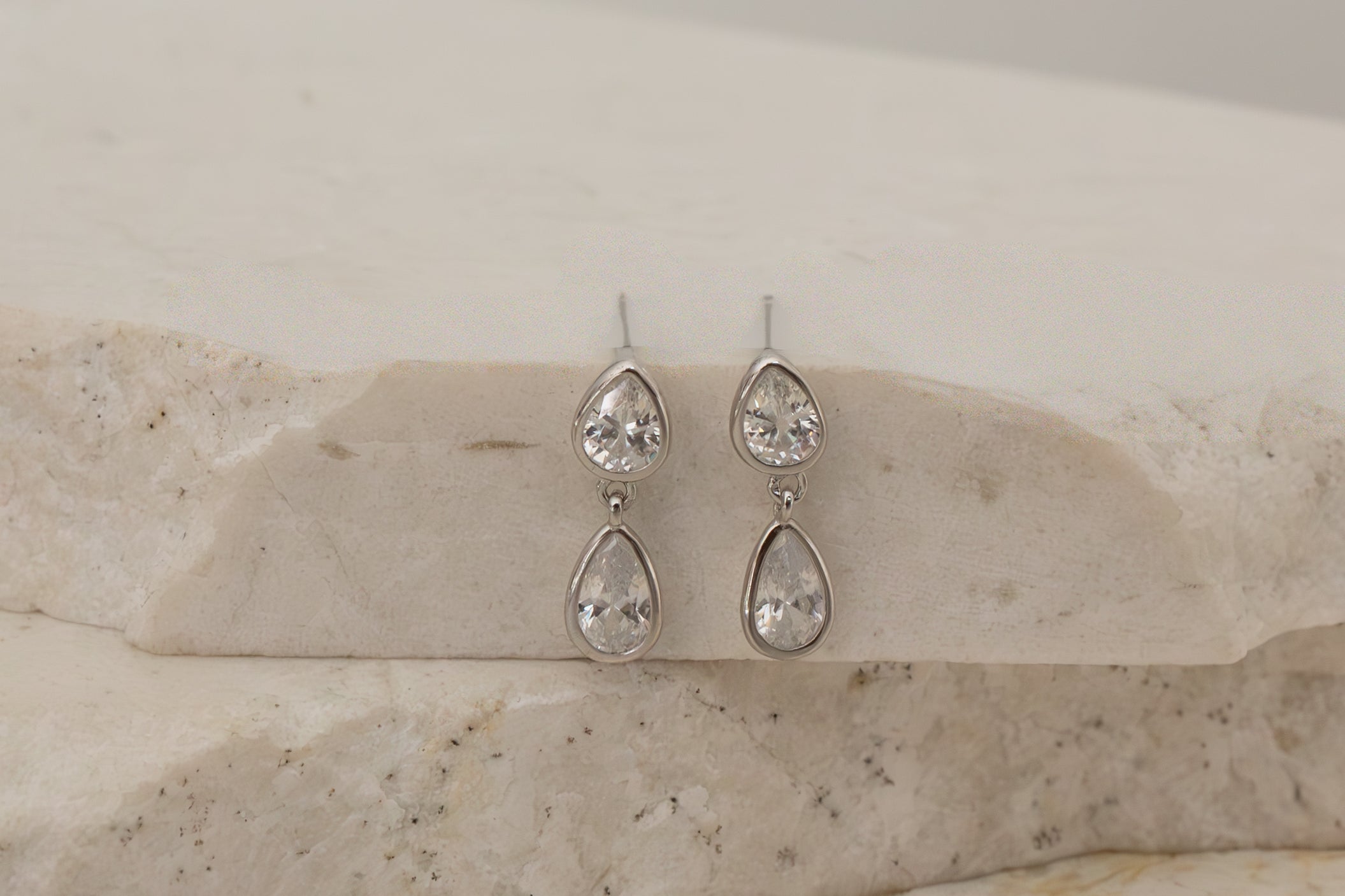 Pair of silver teardrop earrings on a marble surface