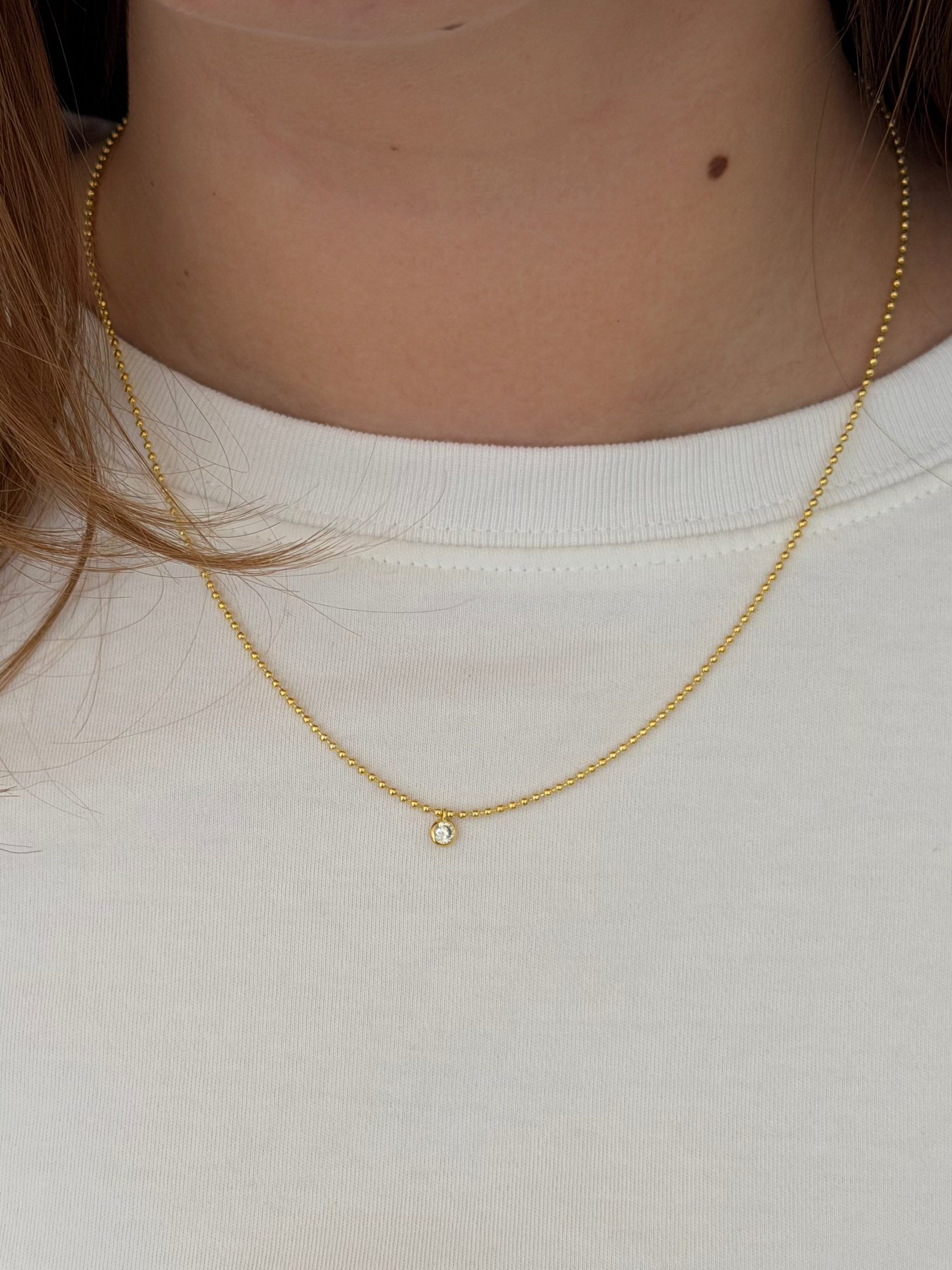 Close-up of a person wearing a gold necklace with a small pendant on a plain background