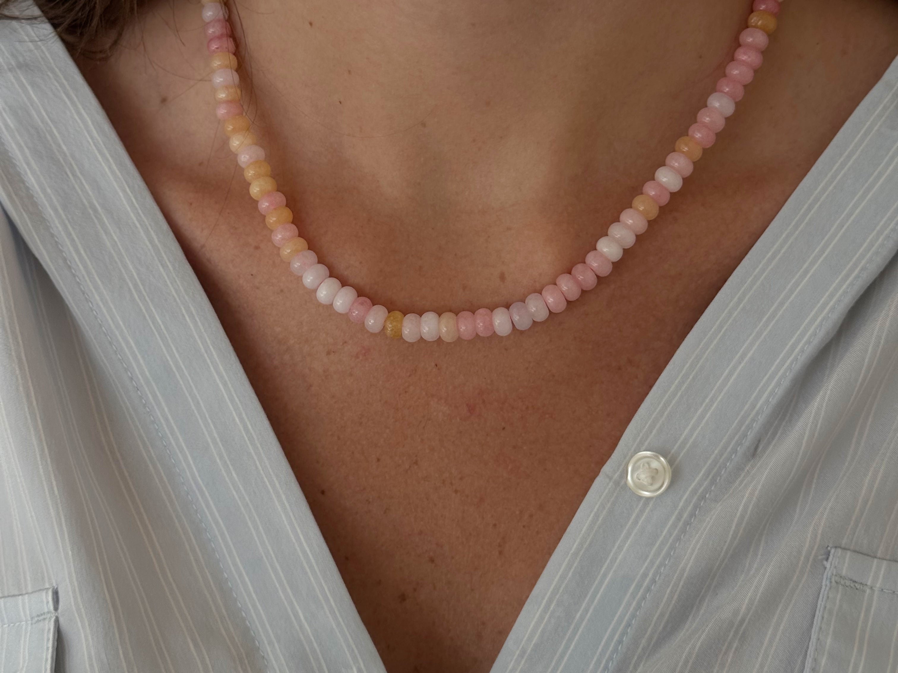 Necklace with pink and white beads worn by a person against a softly blurred background.