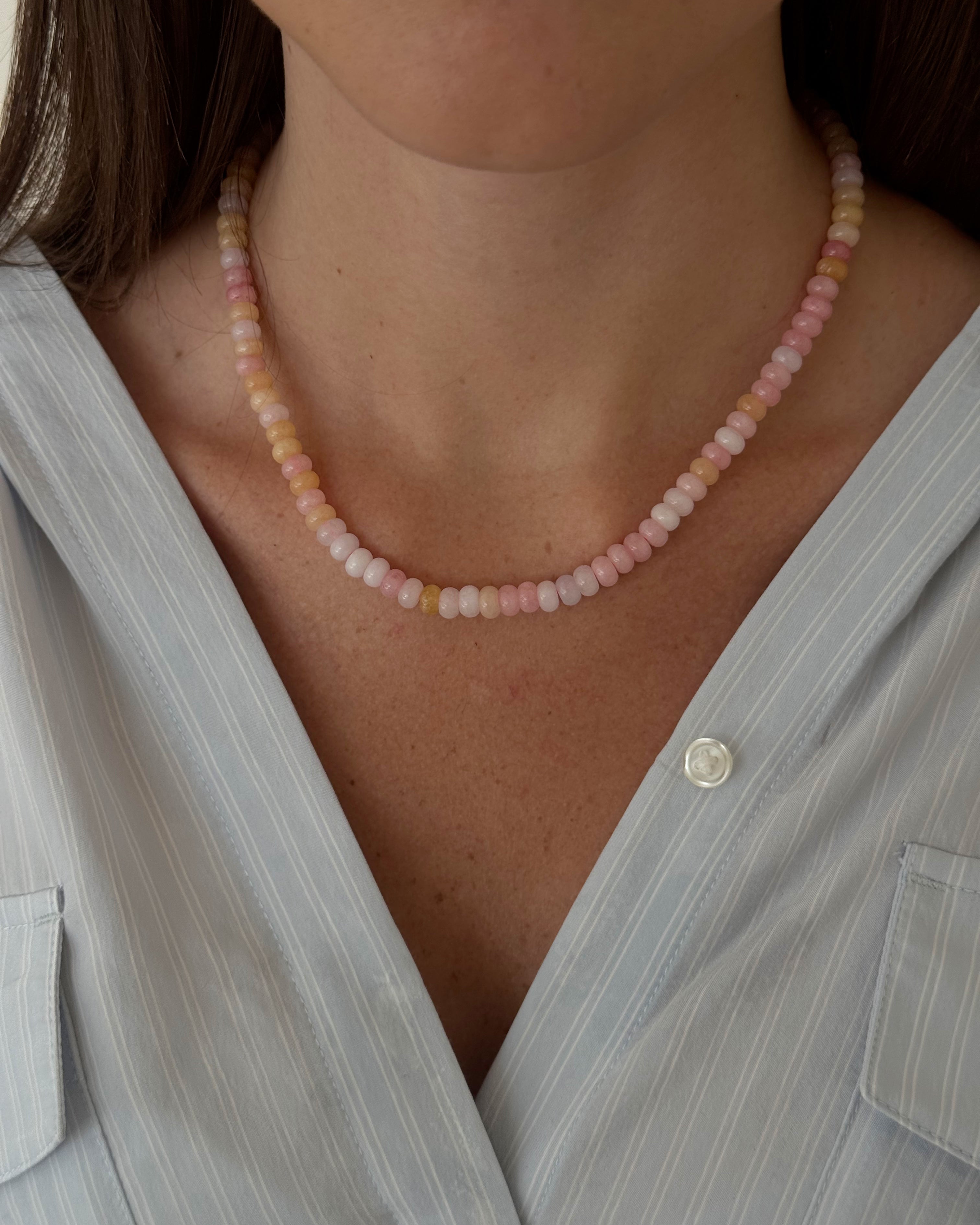 Necklace with pink and white beads worn by a person against a softly blurred background.