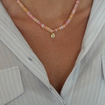 Close-up of a person wearing a pink beaded anklet with a gold charm.