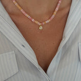 Close-up of a person wearing a pink beaded anklet with a gold charm.