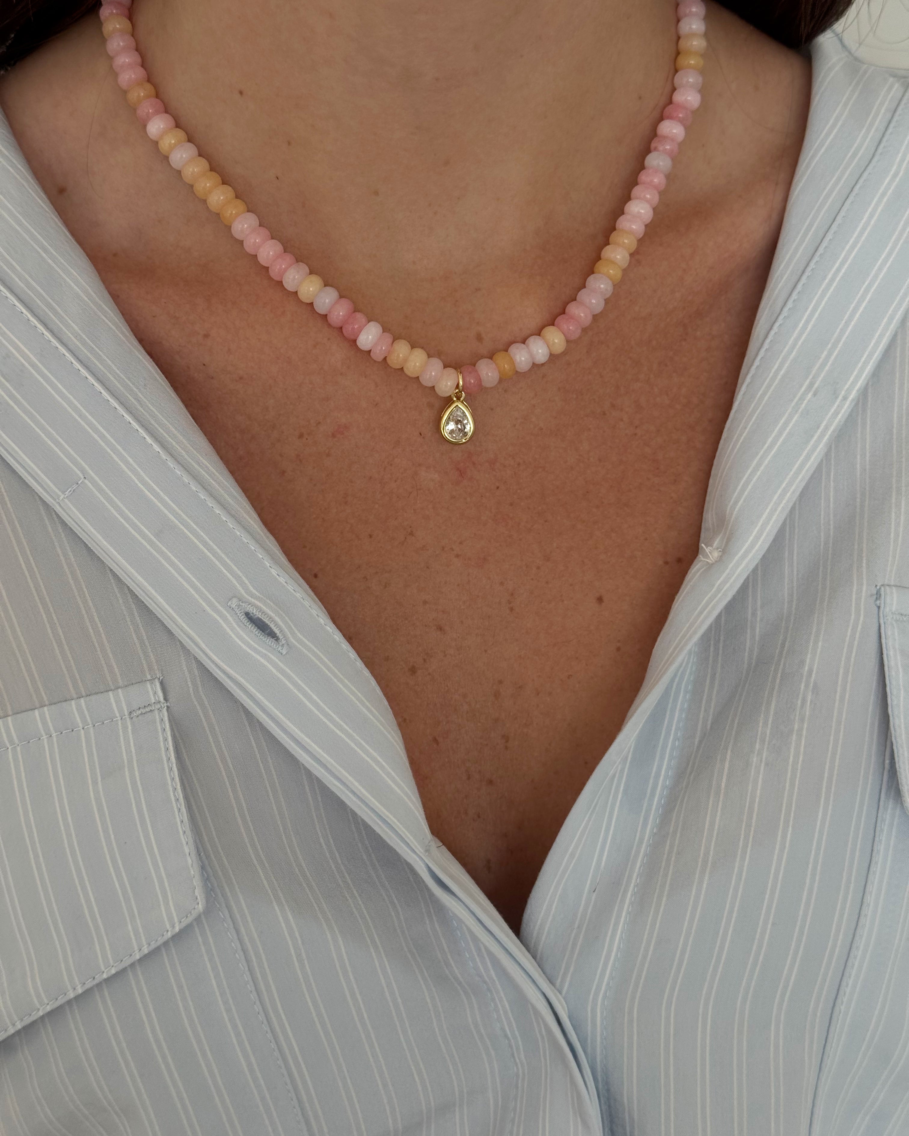 Close-up of a person wearing a pink beaded anklet with a gold charm.